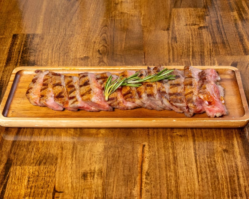 Grilled steak slices with grill marks and rosemary sprigs on a wooden serving tray.