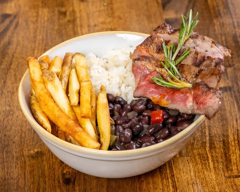 Grilled steak with rosemary, white rice, black beans, and french fries in a bowl.
