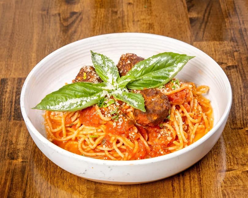 Spaghetti and meatballs in a white bowl, garnished with fresh basil and grated cheese.